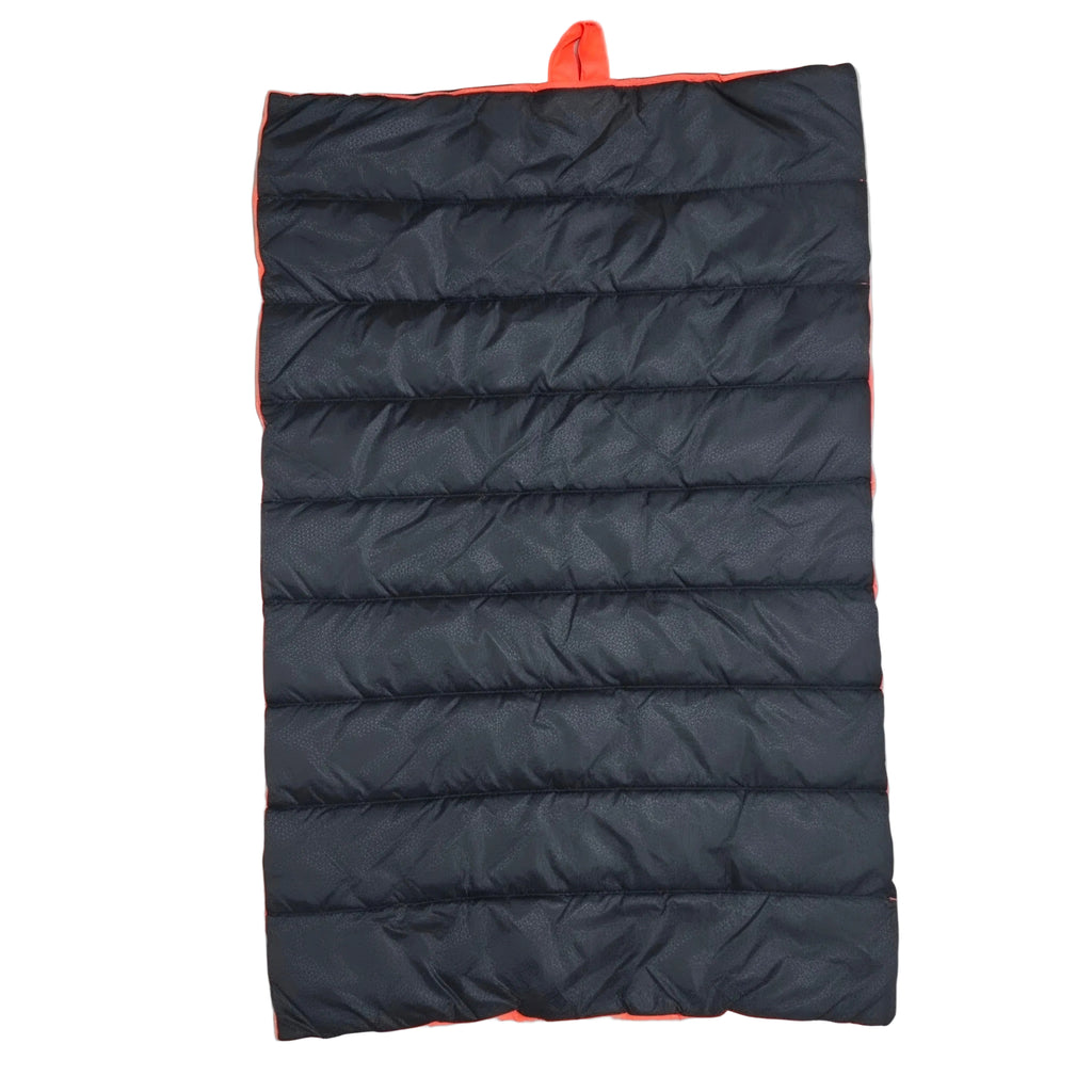 A black puffer sleeping pad with bright orange trim and a top carry loop, laid flat on a light wood floor.